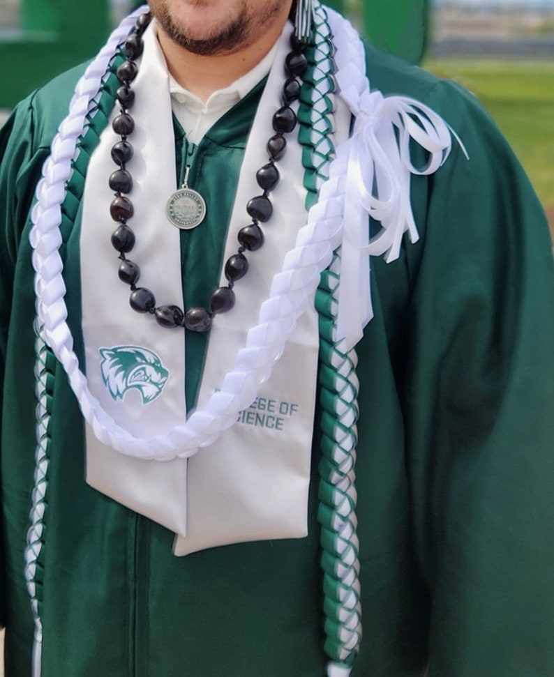 May include: A green graduation gown with a white and green lei, a black beaded necklace with a silver medallion, and a white sash with the text "College of Science".