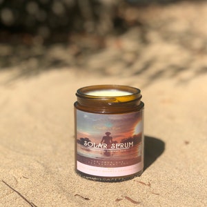 K&ouml;nnte beinhalten: Ein braunes Glas Solar Serum, ein Produkt zur Pflege der Sommerhaut, steht auf Sand. Das Etikett zeigt eine Sonnenuntergangsszene mit einer Person als Silhouette im Wasser. Das Glas enth&auml;lt eine cremige Substanz.