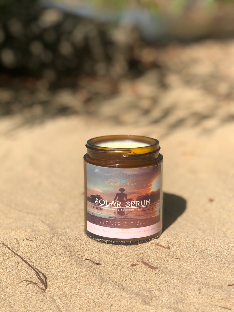K&ouml;nnte beinhalten: Ein braunes Glas Solar Serum, ein Produkt zur Pflege der Sommerhaut, steht auf Sand. Das Etikett zeigt eine Sonnenuntergangsszene mit einer Person als Silhouette im Wasser. Das Glas enth&auml;lt eine cremige Substanz.