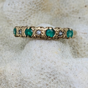 May include: A gold band ring with alternating emerald and diamond stones.