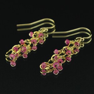 May include: A pair of gold earrings with pink gemstone beads dangling from the bottom. The earrings are made of delicate gold wire and feature a cluster of pink beads at the end of each earring.