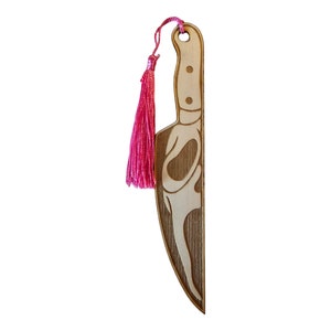 May include: A wooden bookmark shaped like a knife with a pink tassel. The knife has a detailed design and a wood grain texture.
