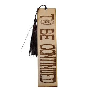 May include: A brown wooden bookmark with a black tassel. The bookmark has the text "TO BE CONTINUED" printed on it.