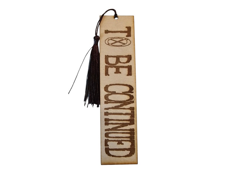 May include: A brown wooden bookmark with a black tassel. The bookmark has the text "TO BE CONTINUED" printed on it.