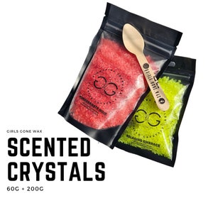 Peut inclure: Deux petits sacs de cristaux parfumés. Le sac de gauche est rouge et porte l'inscription "Pomegranate Noir". Le sac de droite est vert et porte l'inscription "Relaxing Embrace". Les deux sacs portent le texte "Girls Gone Wax" et "Scented Crystals".