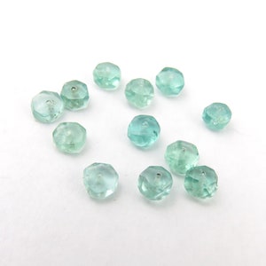 May include: A collection of twelve faceted, light blue gemstone beads. The beads are all approximately the same size and shape, and they have a smooth, polished finish.