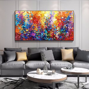 May include: Abstract painting with a colorful, textured, and vibrant design. The painting features a mix of bright colors, including yellow, orange, red, blue, purple, and green. The painting is framed and hanging on a wall in a living room setting.