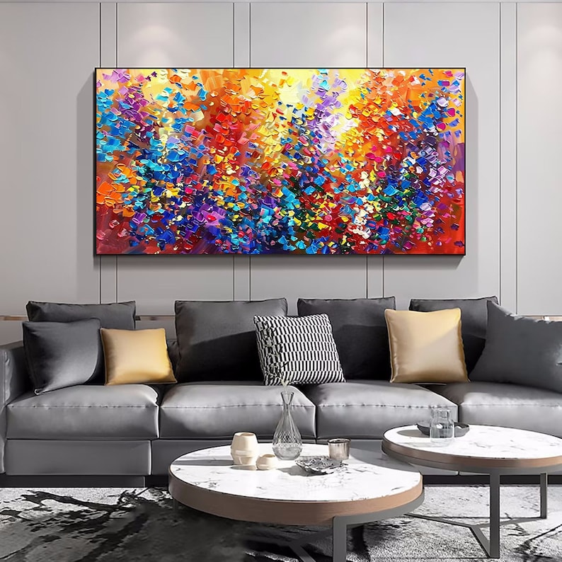 May include: Abstract painting with a colorful, textured, and vibrant design. The painting features a mix of bright colors, including yellow, orange, red, blue, purple, and green. The painting is framed and hanging on a wall in a living room setting.