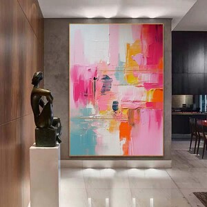 K&ouml;nnte beinhalten: Abstraktes &Ouml;lgem&auml;lde mit goldenem Rahmen. Das Kunstwerk zeigt kr&auml;ftige Pinselstriche in Rosa-, Orange-, Gelb- und Blaut&ouml;nen. Das Gem&auml;lde wird in einem modernen Innenraum mit einer Bronzeskulptur auf einem Sockel ausgestellt.