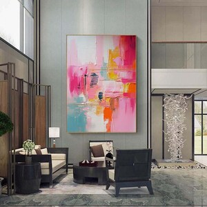 K&ouml;nnte beinhalten: Abstrakte Malerei mit goldenem Rahmen. Das Kunstwerk zeigt kr&auml;ftige Pinselstriche in Rosa, Orange, Gelb und Blau. Das Gem&auml;lde wird in einem modernen Wohnzimmer mit zeitgen&ouml;ssischen M&ouml;beln und Dekoration ausgestellt.