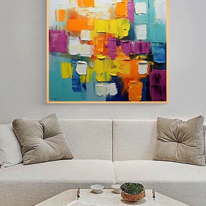 May include: Abstract painting with a colorful geometric design. The painting features squares and rectangles in shades of blue, yellow, orange, purple, and white. The painting is framed in a wooden frame.