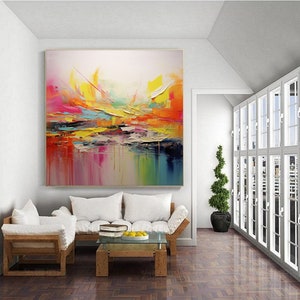 May include: Abstract painting with vibrant colors, including yellow, orange, pink, and blue, on a white background. The painting is displayed on a wall in a living room setting.