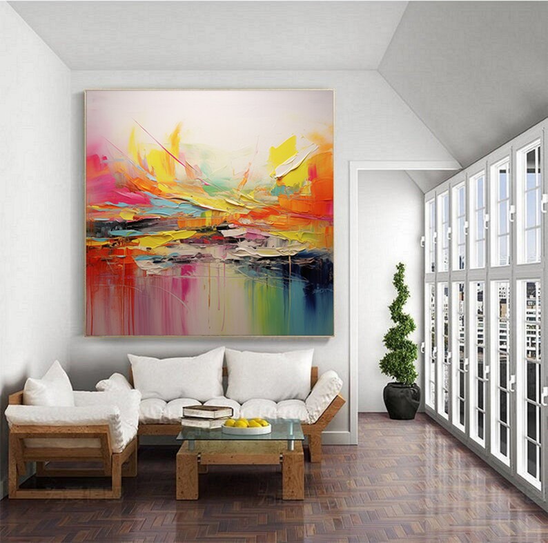 May include: Abstract painting with vibrant colors, including yellow, orange, pink, and blue, on a white background. The painting is displayed on a wall in a living room setting.
