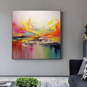 May include: Abstract painting with bold strokes of yellow, orange, pink, blue, and green. The painting has a textured surface and is framed in black.