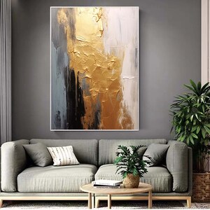 Puede incluir: Pintura abstracta con pintura dorada, negra, blanca y gris. La pintura tiene un aspecto texturizado y est&aacute; enmarcada en un marco blanco.