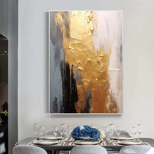 Puede incluir: Pintura abstracta con pintura dorada, negra, blanca y gris. La pintura dorada es texturizada y parece estar goteando por el lienzo.