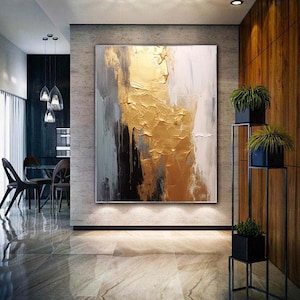 Puede incluir: Pintura abstracta con pintura dorada, negra, blanca y gris. La pintura tiene un aspecto texturizado y se exhibe en una pared de una casa moderna.