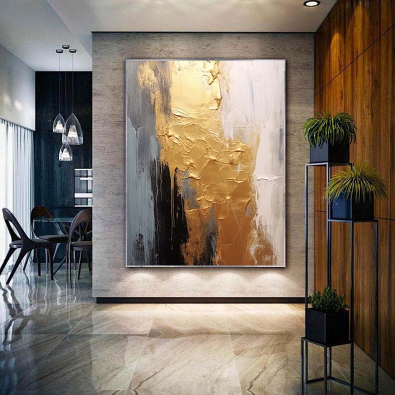 Puede incluir: Pintura abstracta con pintura dorada, negra, blanca y gris. La pintura tiene un aspecto texturizado y se exhibe en una pared de una casa moderna.