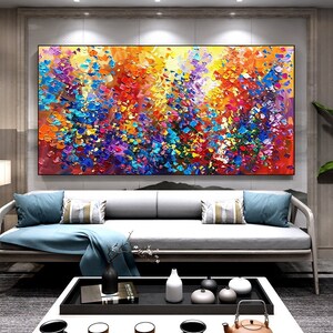 May include: Abstract painting with a colorful, textured, and vibrant design. The painting features a mix of blue, yellow, red, purple, and green colors. The painting is displayed on a wall in a living room setting.