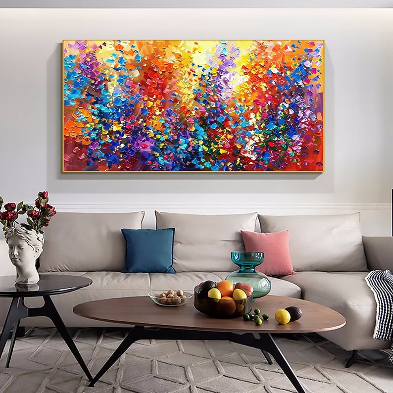 May include: Abstract painting with a colorful, textured, and impressionistic style. The painting features a variety of colors, including red, orange, yellow, green, blue, purple, and white. The painting is framed in a gold frame and is hanging on a white wall above a couch.