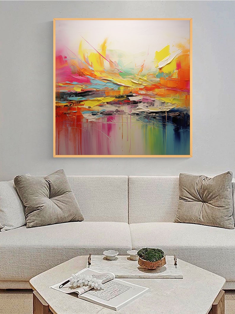 May include: Abstract painting with a colorful, layered design. The painting features shades of pink, yellow, orange, blue, and green. The painting is framed in a light wood frame.