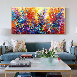 May include: A colorful abstract painting with a textured, impasto style. The painting features a variety of colors, including yellow, orange, red, blue, green, and purple. The painting is framed in a gold frame and is hanging on a white wall above a blue sofa.