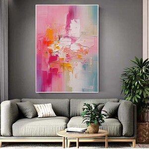 K&ouml;nnte beinhalten: Abstrakte Kunstmalerei mit einer Palette aus Rosa, Orange und Wei&szlig;. Das Kunstwerk weist dicke Pinselstriche auf, die einen strukturierten Effekt erzeugen. Das Gem&auml;lde ist in einem wei&szlig;en Rahmen gerahmt und h&auml;ngt &uuml;ber einem grauen Sofa.