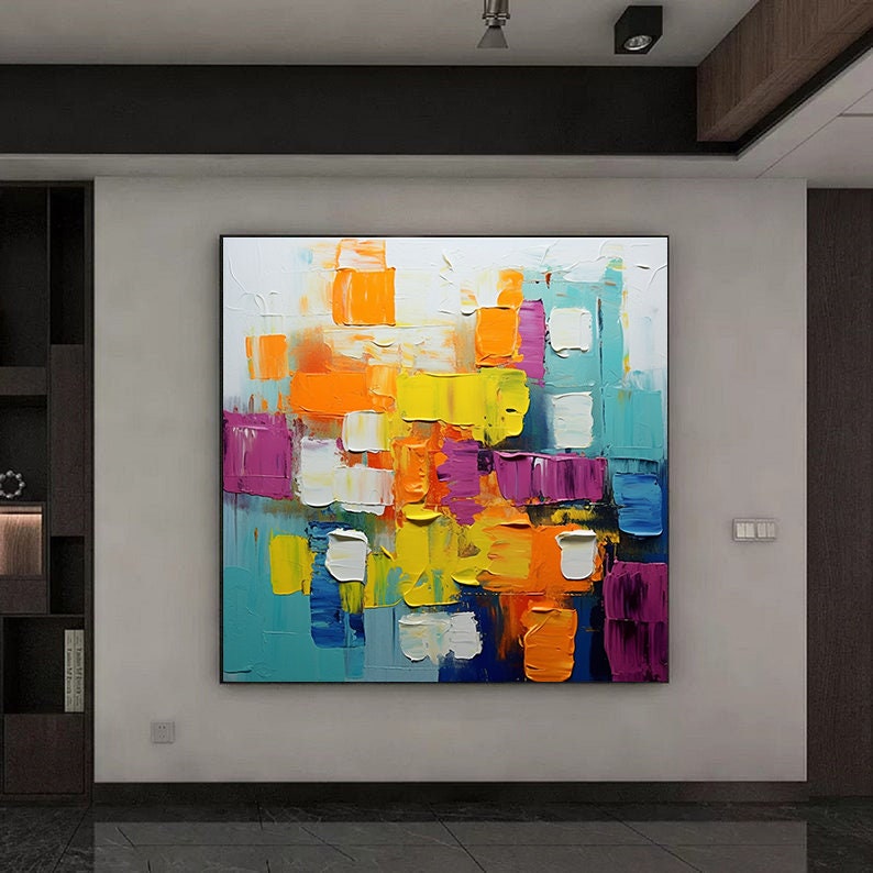 May include: Abstract painting with a colorful geometric pattern. The painting features squares and rectangles in shades of blue, yellow, orange, pink, and white. The paint is applied in thick strokes, creating a textured effect.