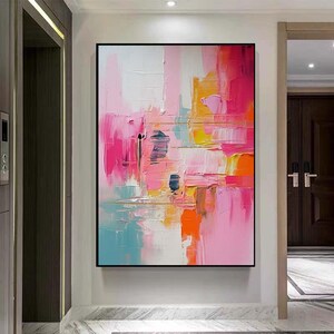 K&ouml;nnte beinhalten: Abstrakte Malerei mit schwarzem Rahmen. Das Kunstwerk zeigt kr&auml;ftige Pinselstriche in Rosa, Orange, Gelb, Blau und Wei&szlig;. Die strukturierte Oberfl&auml;che erzeugt eine dynamische und farbenfrohe Komposition, geeignet f&uuml;r die Inneneinrichtung.