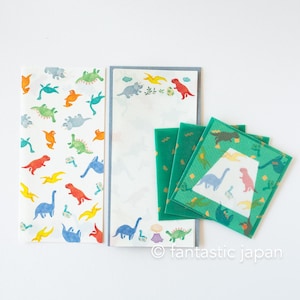 May include: A collection of stationery featuring colorful dinosaur illustrations. The set includes a long notepad, two smaller notepads, and several square coasters. The dinosaurs are in various colors, including blue, red, green, and orange, on a white background.