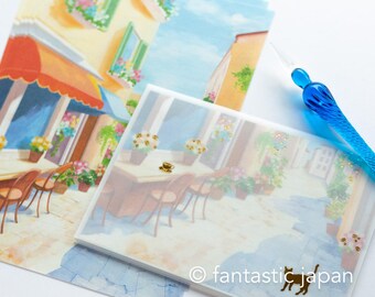 Puede incluir: Un juego de tarjetas en blanco con una ilustración colorida de una cafetería en una ciudad europea. Las tarjetas están decoradas con purpurina dorada y una pequeña ilustración de un gato negro. El texto "fantasticjapan" está impreso en la esquina inferior derecha de la tarjeta.
