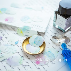 May include: A collection of colorful watercolor stickers with a blue and yellow design. The stickers are on a white surface with a gold metal dish and a blue glass pen.