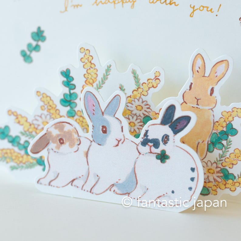 May include: A pop-up card featuring four adorable bunnies surrounded by yellow and green flowers. The card has the text "I'm happy with you!" written on it.