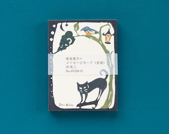Puede incluir: Una tarjeta rectangular con una ilustración de un gato negro, un pájaro y una linterna en una rama de árbol. La tarjeta tiene texto japonés y está sujeta con una banda transparente. El fondo es azul oscuro.