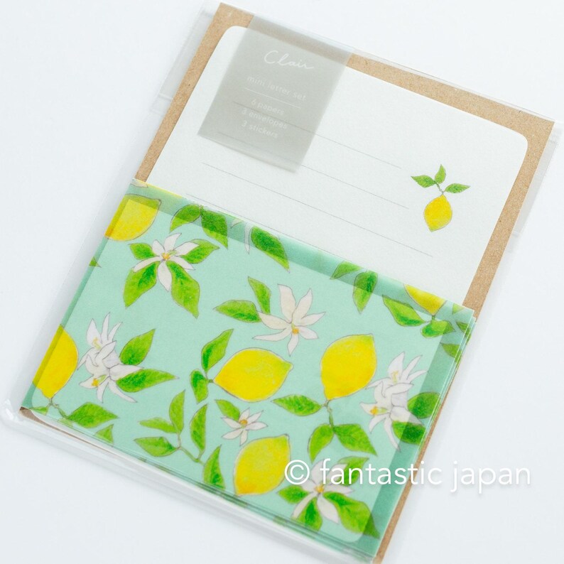 May include: A stationery set featuring a lemon theme. The set includes a notepad with lines and a lemon illustration, and a patterned cover with lemons, white flowers, and green leaves on a light blue background. The text "Clair" is visible.