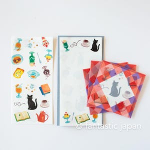 May include: Watercolor stickers and notepaper featuring a cat, books, teacups, and desserts. The stickers are on white paper with colorful illustrations. The notepaper has a light blue border. The image also includes red and purple patterned squares.