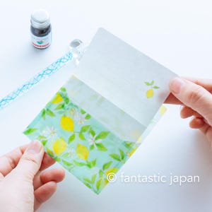 May include: A stationery set featuring a lemon-themed design. The set includes a patterned envelope with lemons and white flowers, and a lined writing sheet. A bottle of ink and a glass pen are also visible.