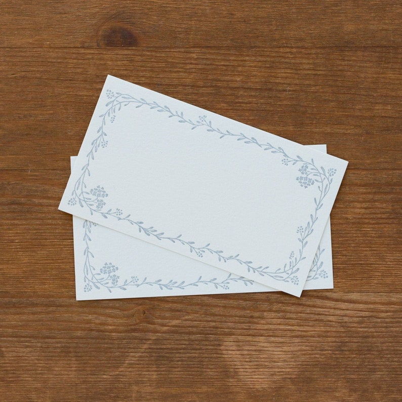 May include: Two blank white cards with a blue floral border. The cards are stacked on top of each other.
