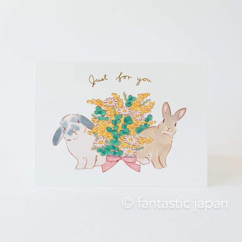 May include: A greeting card featuring a watercolour illustration of two rabbits holding a bouquet of yellow and white flowers. The card has the text "Just for you" written in gold lettering.