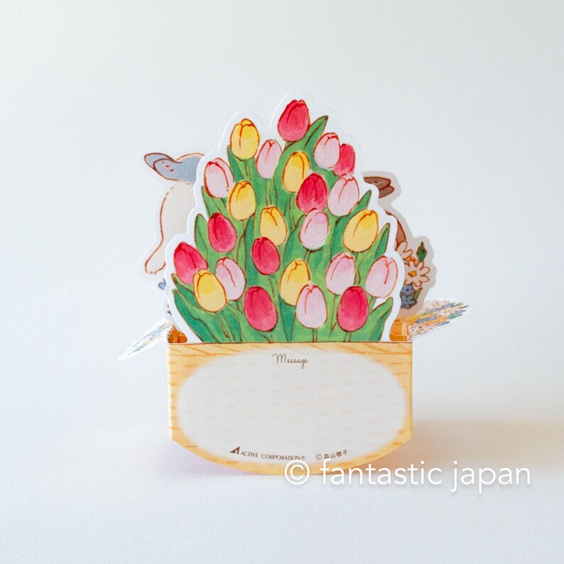 May include: A pop-up card with a bouquet of pink, yellow, and red tulips in a wooden planter. The card has a space for a message and says "Message" on the front.