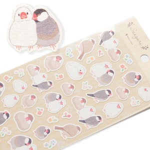 Könnte beinhalten: Eine Bogen mit Aufklebern mit niedlichen Illustrationen von Finken in verschiedenen Posen. Die Aufkleber befinden sich auf einem beigefarbenen Hintergrund mit kleinen Blumenmustern. Der Bogen ist oben rechts mit "Saeguri" beschriftet.