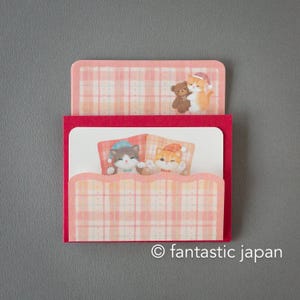 Puede incluir: Un tarjetero de papel rojo y rosa con un estampado de cuadros. El tarjetero presenta ilustraciones de gatos de dibujos animados con gorros de dormir y un pequeño osito de peluche. El texto "fantastic japan" está impreso en la parte inferior.