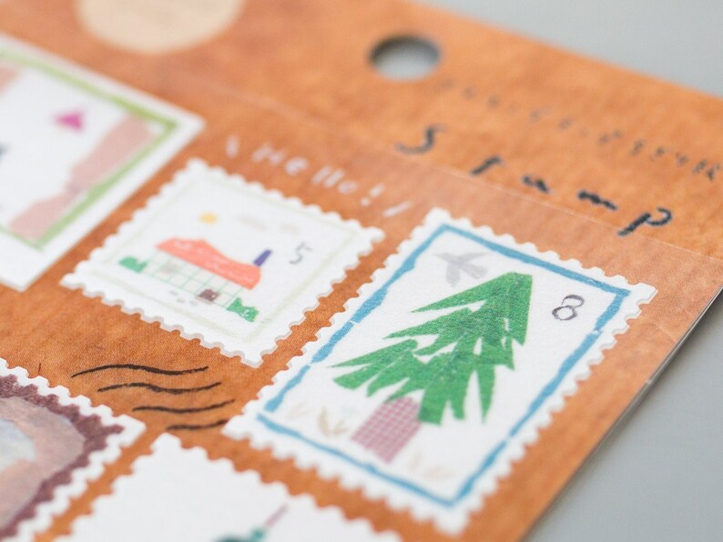 May include: A sheet of decorative stamps with a brown background. The stamps feature illustrations of a house, a tree, and a bird. The text "Hello!" and "Adventure Stamp" are printed on the sheet.