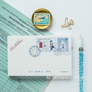 Puede incluir: Un paquete de 80 hojas de papel de cartas en blanco con un diseño ilustrado en azul y blanco de una oficina de correos y un pájaro. El texto "雲の上郵便局一筆箋" está impreso en la parte delantera del paquete.