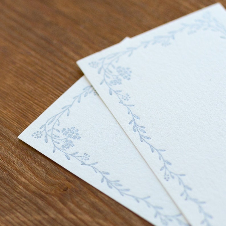 May include: Two white cards with a blue floral border. The cards are blank and ready for writing.