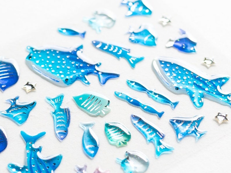May include: A collection of blue and white whale shark and fish stickers. The stickers are made of a clear, glossy material and have a 3D effect.