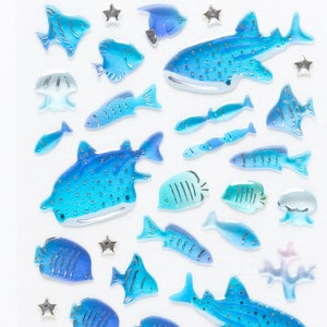 May include: A sheet of blue and silver whale and fish stickers. The stickers are on a white background.