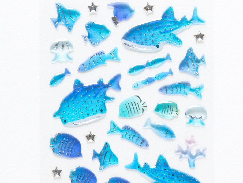 May include: A sheet of blue and silver whale and fish stickers. The stickers are on a white background.