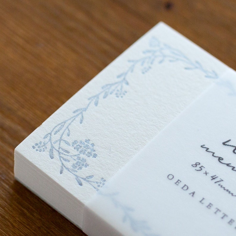 May include: A stack of white note cards with a blue floral design on the edge. The cards are 85 x 47 mm and are labeled "OEDA LETTERS".