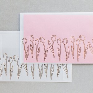 Puede incluir: Dos sobres blancos con un sobre rosa en la parte superior. Los sobres tienen un dise&ntilde;o de tulipanes en pan de oro a lo largo del borde inferior.